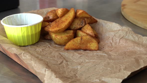 The Chef in Black Gloves Puts a Burger on a Board with Rustic Potatoes and Sauce alt