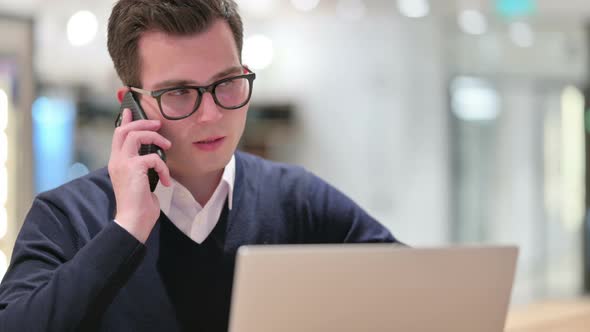 Young Businessman with Laptop Talking on Smartphone  alt