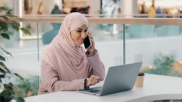 Arab Multitasking Woman Sitting Working on Laptop Talking on Mobile Telephone Remotely Consulting alt