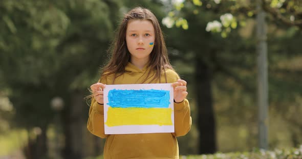 Serious face of a little girl. The child's cheeks are painted with the yellow and blue colors 