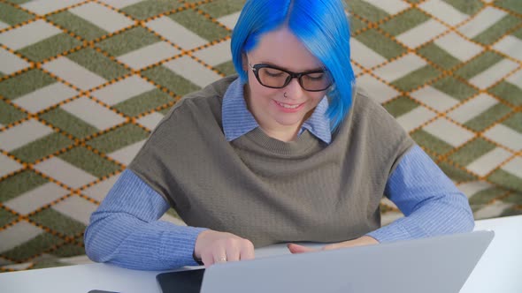 Nerd girl with blue hair working on notebook computer at home during lockdown in 4k video alt
