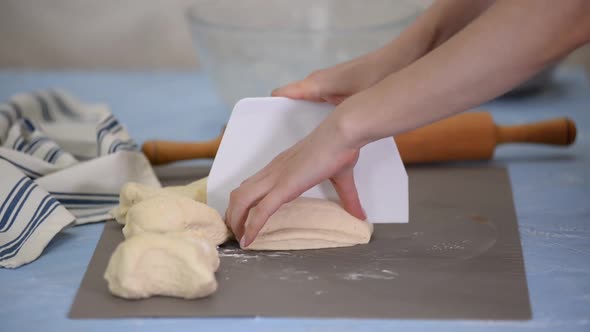 A woman cuts the dough on a table. Making yeast buns.