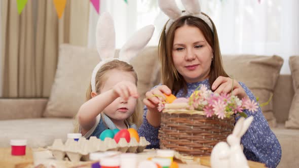 Mom and Little Daughter with Rabbit Ears Celebrate Easter and Lay Painted Eggs alt