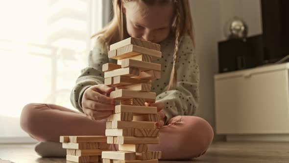 Child plays a board game, kid builds from wooden bricks blocks and the construction tower falls alt