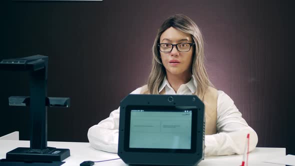 Female Humanlike Robot Is Sitting Behind the Desk and Talking alt