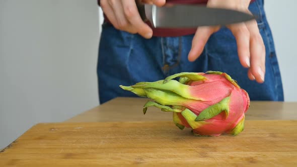 Female Hands is Cutting a Dragon Fruit or Pitaya with Pink Skin and White Pulp with Black Seeds on alt