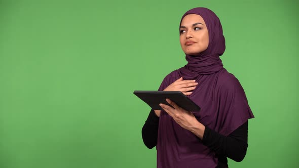 A Young Beautiful Muslim Woman Scrolls on a Tablet and Thinks with a Smile  Green Screen Background