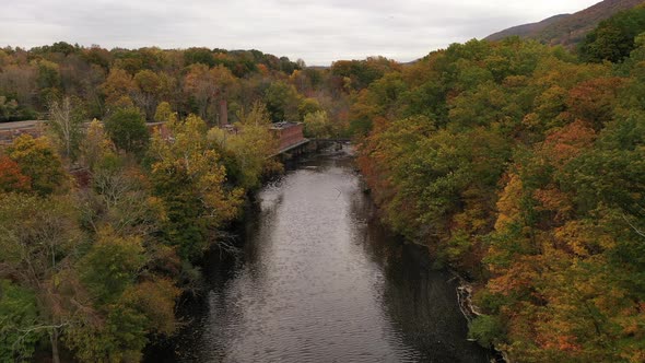 An aerial shot of the colorful fall foliage in upstate NY. The camera dolly in over a black river wi alt