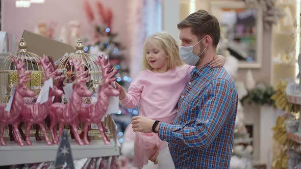 Father in Medical Mask with Daughter in Shopping Mall Choose Home Decorations for Christmas alt