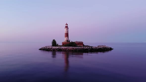 Small artificial island with old light tower, aerial shot in dusk, many birds