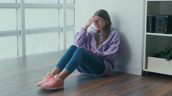 Sad Young Woman Sits on the Floor Looking at Cellphone Screen and Begin Cry alt