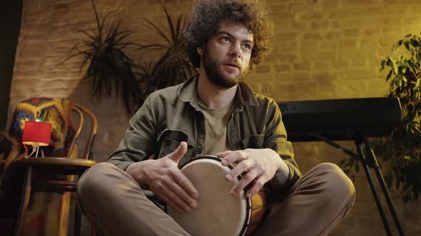 Young Focused Man Musician Beating Drum at Home Practicing Rhythm of New Melody Zoom Out and in alt