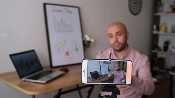 Young man lecturing by recording video on his mobile phone, producing content for social media