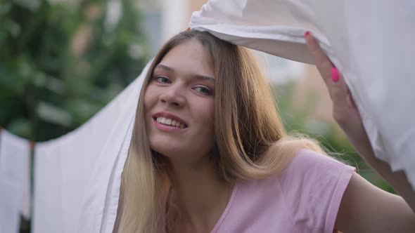 White Clean Laundry Hanging on Rope Outdoors with Cheerful Young Caucasian Woman Peeking Smiling alt