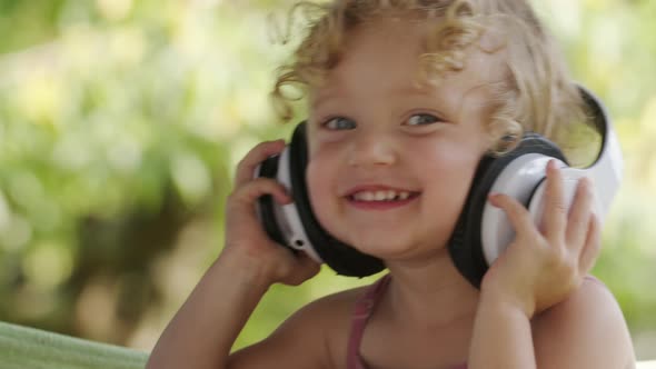 Happy smiling little baby girl listening to music wearing headphones, close-up portrait of funny kid