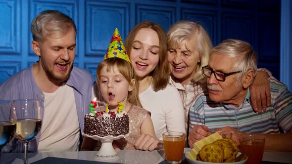 Girl Celebrating Birthday Party with Parents Senior Grandparents Family Blowing Out Candles on Cake alt