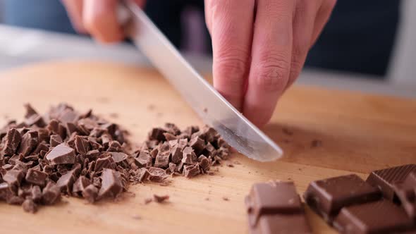 Woman Chopping Black Dark Chocolate on Wooden Cutting Board alt