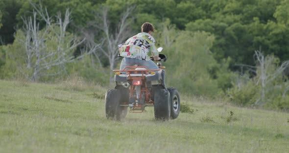 Young Boy on an ATV in a Meadow Near the Forest alt
