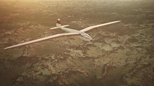 The white sailplane calmly gliding in the sky over the snow-covered mountains. alt