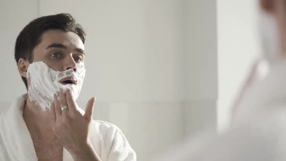 Closeup Reflection in Mirror of Confident Handsome Young Man Applying Shaving Foam alt