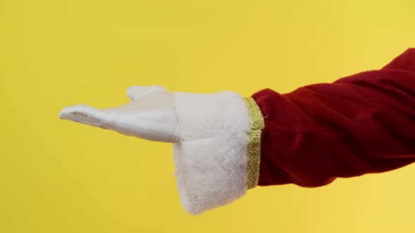 Close-up of Santa Claus gloved hand show giving gesturing on yellow background.