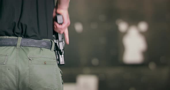 Back View Closeup of a Man Pulling a Pistol Out of Its Holster and Firing a Shot at a Shooting Range alt