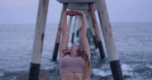 Young Woman Practicing Yoga and Stretching During a Sunset on the Beach alt