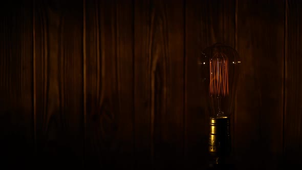 Old Vintage Edison Light Bulb Glowing on Background of Wooden Planks alt