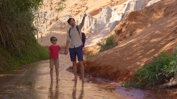 A Family Walks Along a Red Canyon or Fairy Stream at the Border of Desert in the Mui Ne Village in alt
