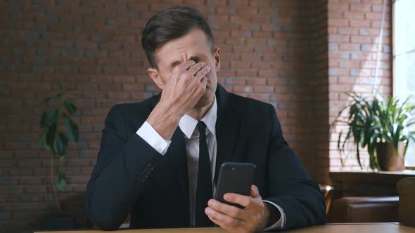 Tired and Stressed Businessman Using Smartphone Feeling Headache