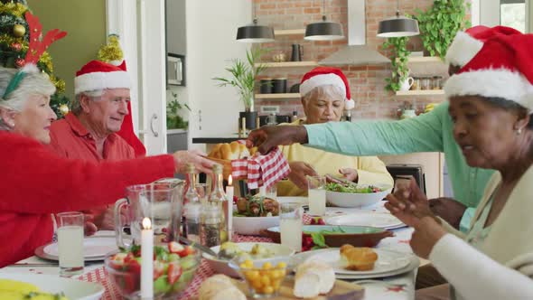 Group of happy diverse senior friends in santa hats making a toast at christmas dinner table at home alt