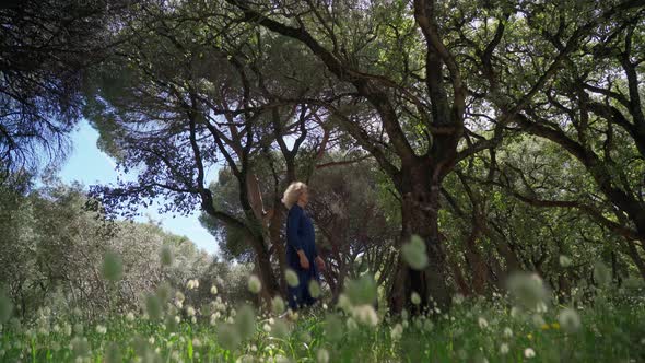 A European Woman Middleaged in a Dress Walks on a Prak with Tall Grass alt