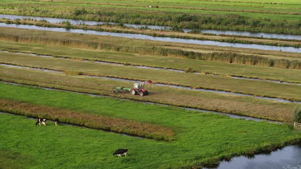 Small agriculture tractor working in green fields surrounded by water canals, aerial view alt