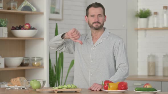 Young Man Showing Thumbs Down While Standing in Kitchen alt