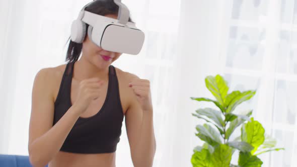 Athletic Asian young woman in sportswear using VR virtual reality glasses headset workout boxing alt