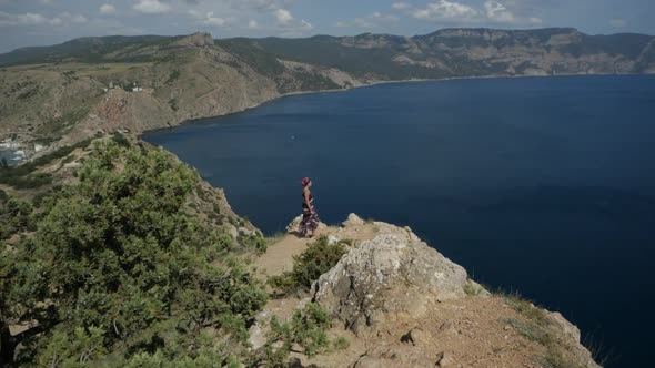 Woman in a Dress Stands on Top of the Slope Against the Backdrop of the Sea Bay