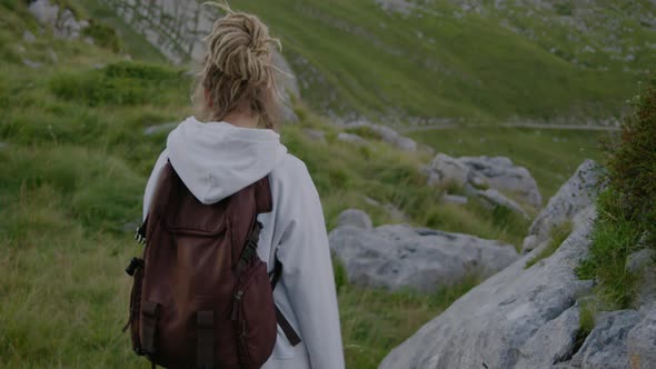 Back view of travel woman with dreadlocks and backpack walking alt