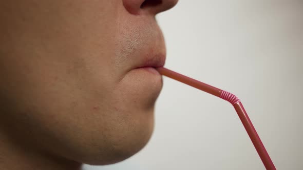 Man drinking a drink from a plastic cocktail tube, close up, side view alt
