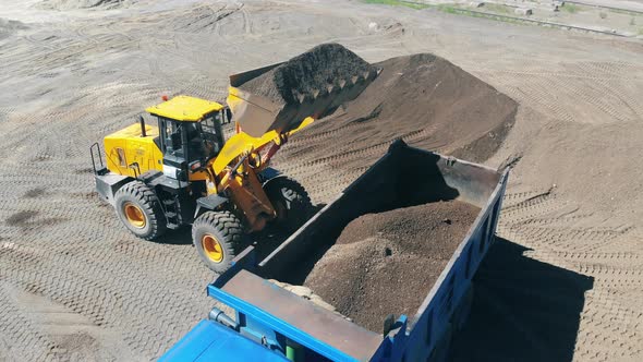 Tractor with a Bucket Loads a Machine with Sand and Rubbles alt