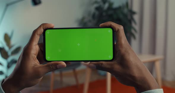 African American Man Resting on Couch at Home and Using Modern Smartphone alt