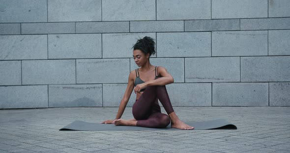 AfricanAmerican Woman Does Fish Lord Asana Sitting on Mat alt