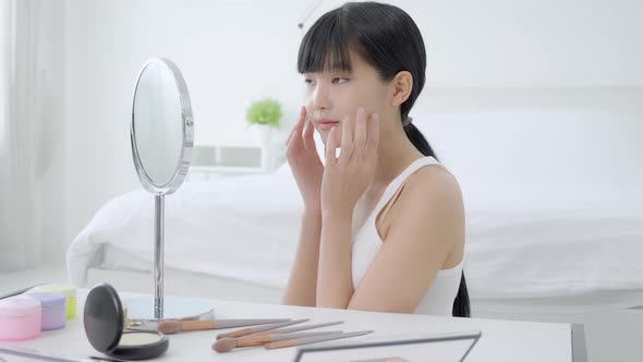 Beautiful face of young asian woman with happy smiling and touch cheek looking mirror with charming. alt