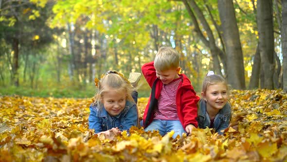 A little boy and two girls play in the autumn Park with yellow leaves lying on the ground.