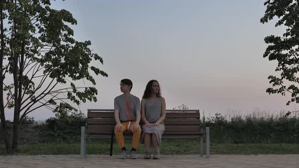 Young Couple Sitting on a Bench Facing the Camera alt