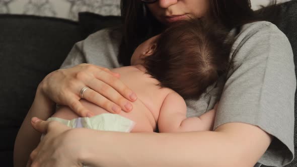 Authentic young mother holds newborn baby on her chest, strokes his back while he sleeps alt
