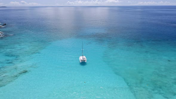 Aerial View of Lonely Luxury Catamaran Yacht in Crystal Clear Blue Lagoon with Reflected Light alt