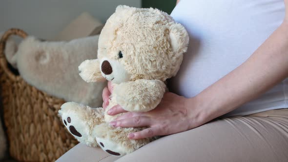 Pregnant girl in a white T-shirt holding a teddy bear and waiting for the baby.
