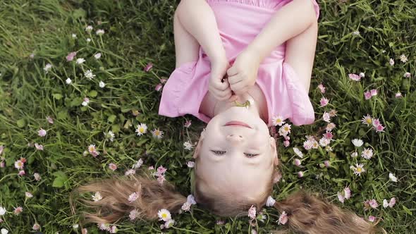 Smiling Little Cute Baby Girl Lying on Green Grass Holding Flowers Looking at Camera