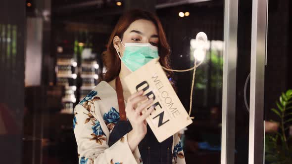 Business owner attractive young mixed race woman in apron hanging we're open sign alt