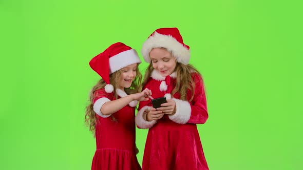 Two Baby Girls Look at the Pictures on the Phone and Laugh. Green Screen. Slow Motion alt
